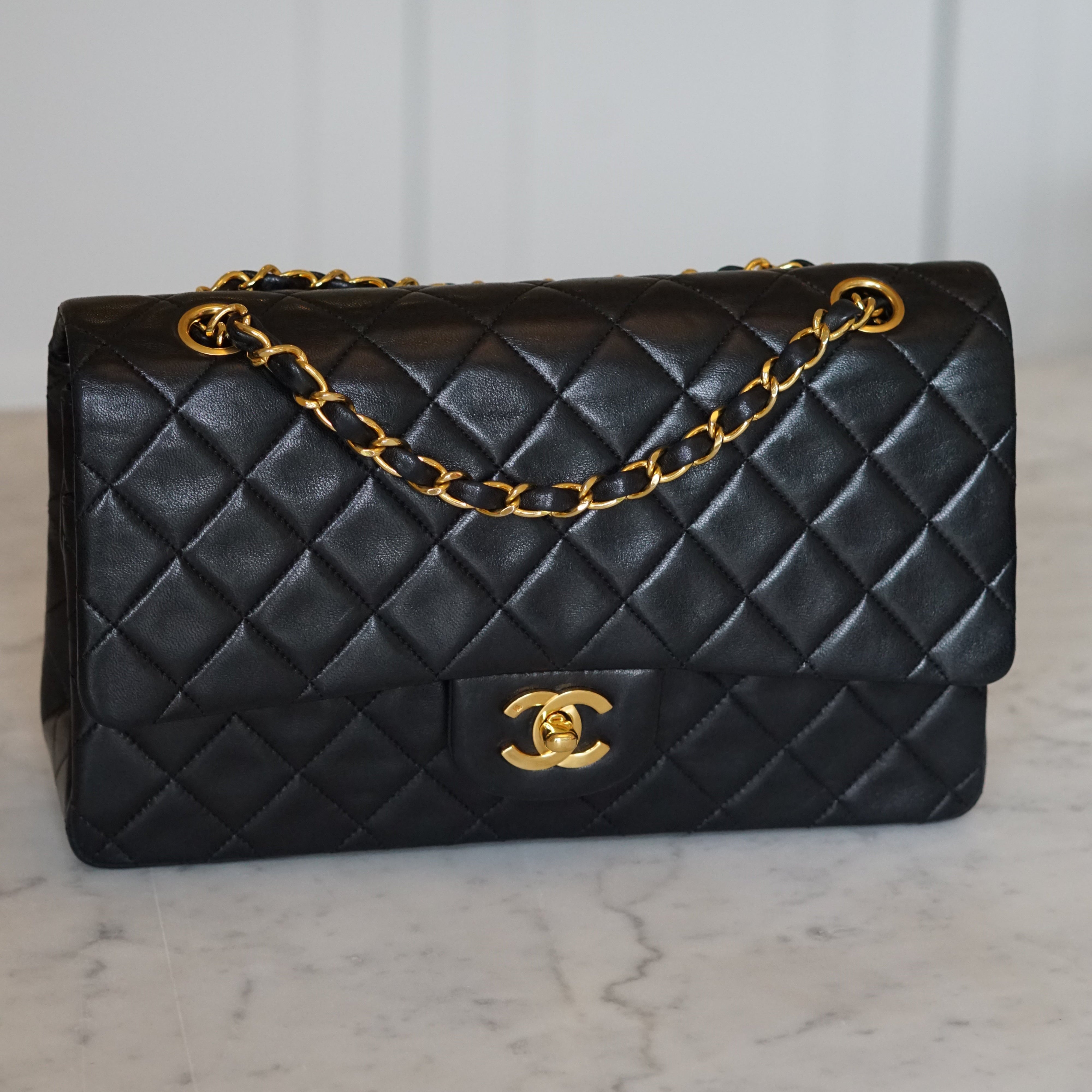 Black quilted handbag with gold chain and clasp on a light gray background