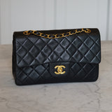 Black quilted handbag with gold chain and clasp on a light marble background