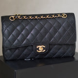 Black quilted handbag with gold chain and clasp on a light gray background