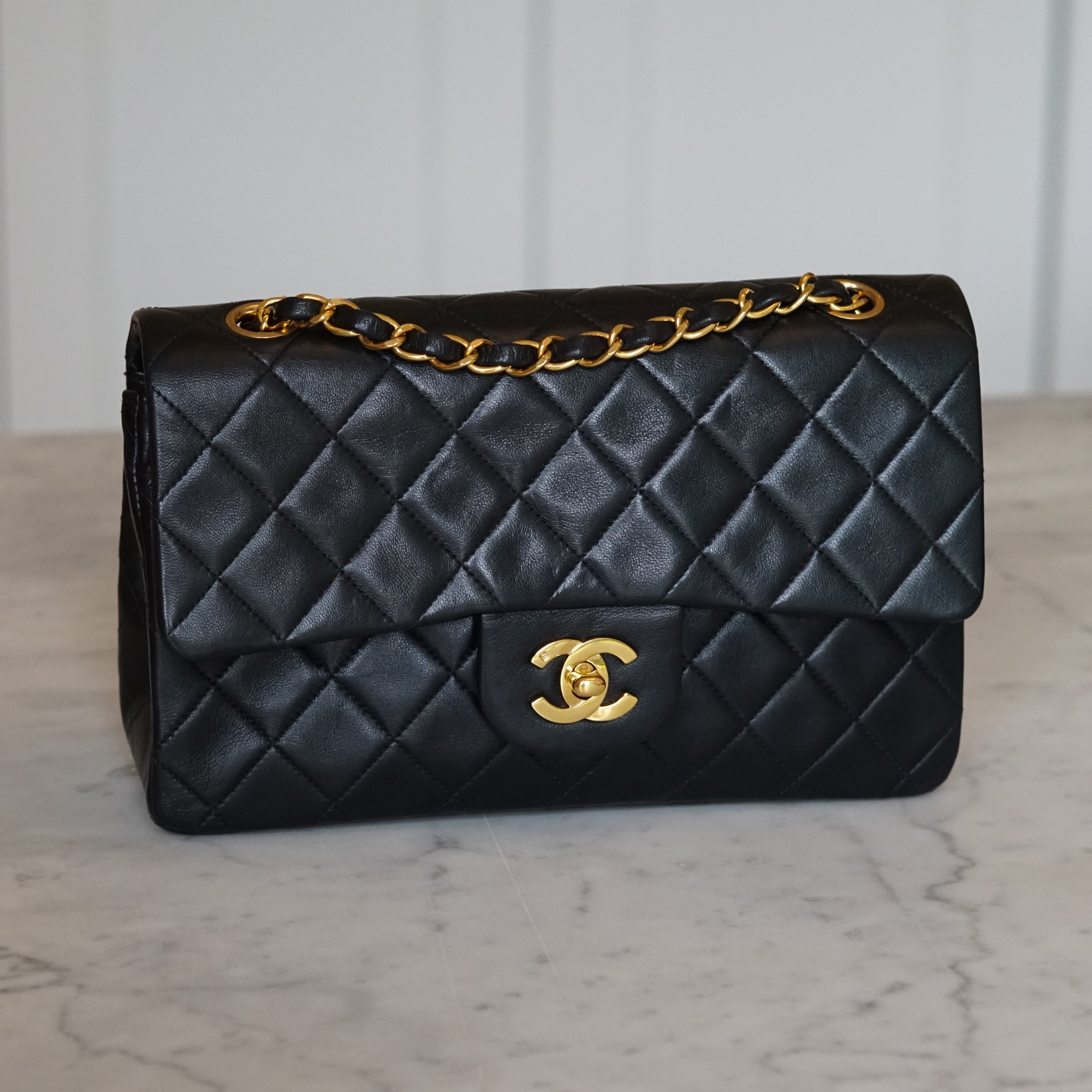 Black quilted handbag with gold chain and clasp on a light marble background