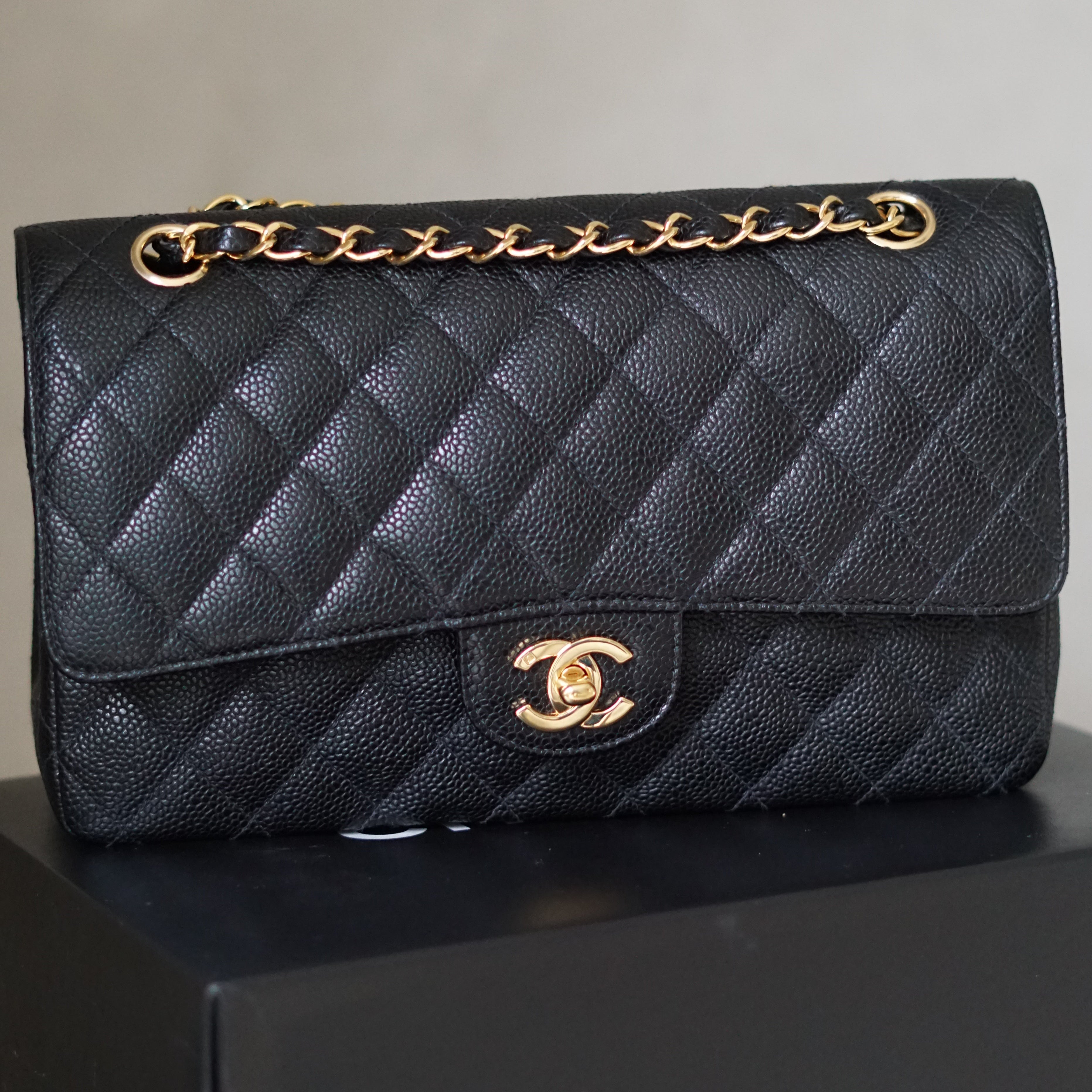 Black quilted handbag with gold chain and clasp on a light gray background